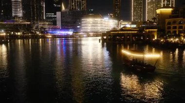 Huzurlu bir gece sahnesi, sakin bir nehirde yüzen bir tekne gibi gözler önüne seriliyor. Şehir ışıkları sudan yansıyarak rüya gibi bir ortam yaratıyor.