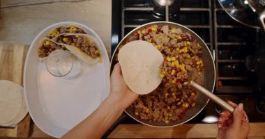 Videoda mutfakta lezzetli taco yapan biri var. Sıcak tavada renkli malzemeler pişirip tortillaları doldurarak davetkar bir atmosfer yaratıyorlar.
