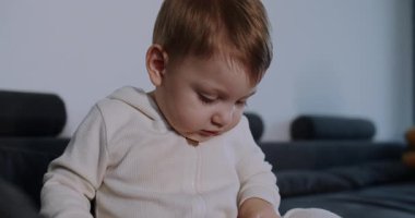 Çekici bir videoda, bir çocuk yakınlarda bir kitap okurken, koltukta oyuncaklarla oynayan, zemini keşfeden ve blokları kullanan bir bebek görülüyor.