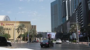 Videoda yüksek binalar, araçlar ve mavi-beyaz taksiler ve siyah bir arabanın yer aldığı canlı bir şehir caddesi yer alıyor.