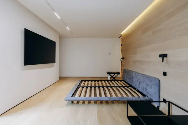 Rahat bir yatak odası ve duvarda eğlence amaçlı döşenmiş düz ekran bir televizyon.