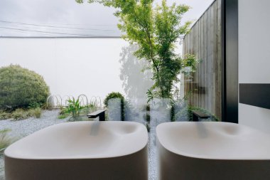 Güzel tasarlanmış bir banyoda stratejik olarak yerleştirilmiş iki güzel lavabo var. Dışarıda çiçek açan bahçenin güzel bir manzarası var.