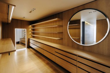 Zarif ahşap rafların olduğu geniş bir dolap var. Estetiği geliştiren güzel yuvarlak bir ayna eşliğinde ustalıkla hazırlanmış.