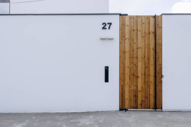 Tahta kapılı beyaz bir duvar var, ve bu kapıda, 27 numara belirgin bir şekilde tanımlama amacıyla sergileniyor.