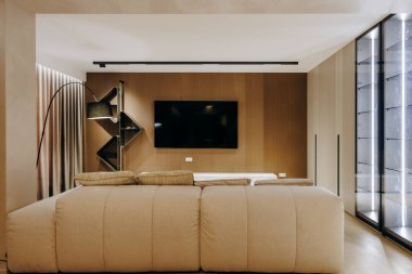 Konforlu ve davetkar bir oturma odasında, göze çarpan bir şekilde yerleştirilmiş şık bir kanepe var, ve yukarıdaki duvarda, parlak bir düz ekran televizyon monte ediliyor.