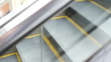 Bu video, yoğun bir alışveriş merkezindeki yürüyen merdivenleri gösteriyor. Onlara binen ve canlı atmosferi yakın çekimle aydınlatan bir kişi var.
