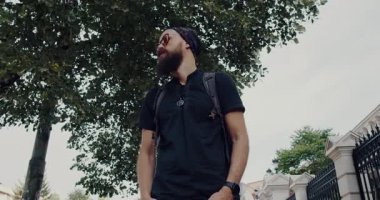 Bu büyüleyici videoda, sakallı bir adam doğa ve şehir yaşamını yansıtıyor, görkemli bir ağaçtan güneşli bir kaldırıma geçiş yapıyor, macera ve birlikte yaşam temalarını keşfediyor.