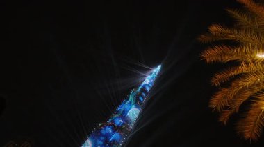 Canlı bir şehrin ufuk çizgisi en yüksek aydınlatılmış bina, yanıp sönen ışıklar ve sallanan bir palmiye ağacına ev sahipliği yapar ve canlı şehir atmosferini yükseltir.