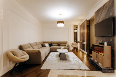 Oturma odasında rahat bir kanepe, rahat bir sandalye, modern bir televizyon ve hoş geldin şöminesi var.