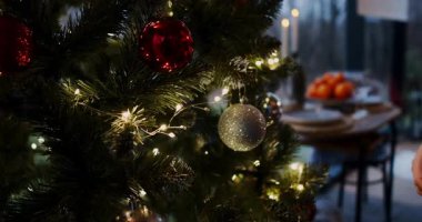 Sıcak bir oturma odası tatil ruhuyla doludur. Bir kadın bir Noel ağacını pırıltılı ışıklar ve renkli süslerle süsler.
