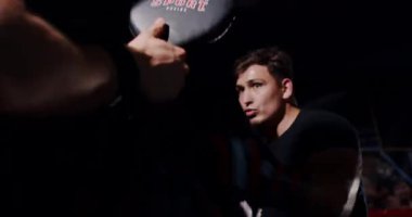 Loş bir boks ringinde, kararlı bir adam yeteneklerini yoğun bir maçta sergiliyor, gölgeler rakibine odaklandıkça dramayı arttırıyor.