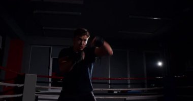 Loş bir boks ringinde, kararlı bir adam yeteneklerini yoğun bir maçta sergiliyor, gölgeler rakibine odaklandıkça dramayı arttırıyor.