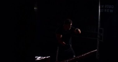 Loş bir boks ringinde, kararlı bir adam yeteneklerini yoğun bir maçta sergiliyor, gölgeler rakibine odaklandıkça dramayı arttırıyor.