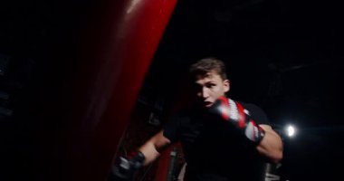 Loş bir boks ringinde, kararlı bir adam yeteneklerini yoğun bir maçta sergiliyor, gölgeler rakibine odaklandıkça dramayı arttırıyor.