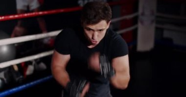 Loş bir boks ringinde, kararlı bir adam yeteneklerini yoğun bir maçta sergiliyor, gölgeler rakibine odaklandıkça dramayı arttırıyor.