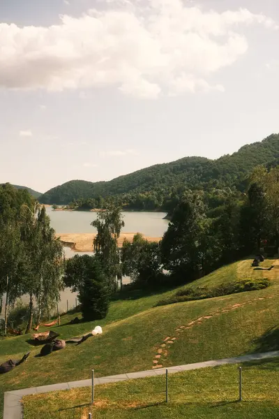 Resimli bir manzara, arka planda yükselen görkemli dağları olan sakin bir gölü sergiliyor ve çarpıcı bir doğal manzara yaratıyor.