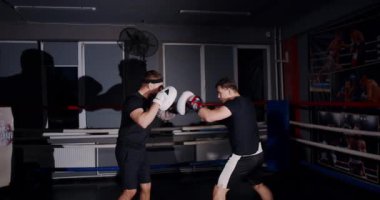 Loş bir boks ringinde, kararlı bir adam yeteneklerini yoğun bir maçta sergiliyor, gölgeler rakibine odaklandıkça dramayı arttırıyor.