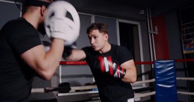 Loş bir boks ringinde, kararlı bir adam yeteneklerini yoğun bir maçta sergiliyor, gölgeler rakibine odaklandıkça dramayı arttırıyor.