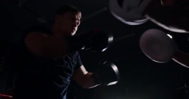 Loş bir boks ringinde, kararlı bir adam yeteneklerini yoğun bir maçta sergiliyor, gölgeler rakibine odaklandıkça dramayı arttırıyor.