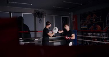 Loş bir boks ringinde, kararlı bir adam yeteneklerini yoğun bir maçta sergiliyor, gölgeler rakibine odaklandıkça dramayı arttırıyor.