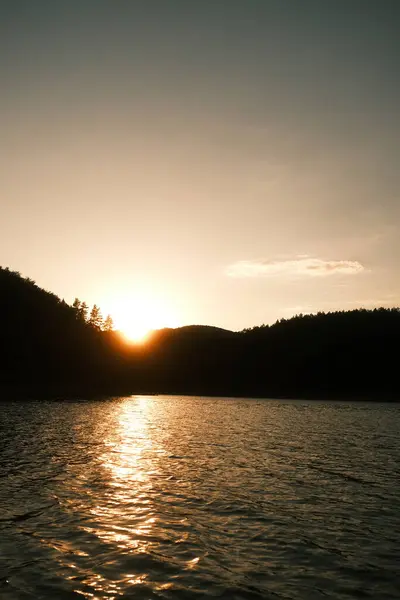 Güneş zarif bir şekilde dingin bir gölün üzerinde batarken, muhteşem dağlar arka planda dikilir ve güzel bir doğal manzara yaratır.