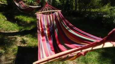 Sakin bir ormanlık alanda, ağaçlardan sarkan canlı hamaklar rahatlamaya davetiye çıkarır. Bir insan bir tanesinin içinde uzanır, doğal huzurun tadını çıkarır.