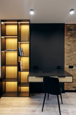 Minimalist bir masa ve odaları estetik hale getiren aydınlatılmış bir kitaplığın yer aldığı modern bir çalışma alanı.