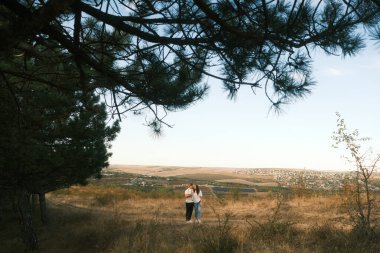 A couple delights in a tranquil stroll amid nature, surrounded by majestic pine trees and gentle, rolling hills