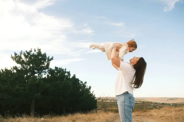 A truly heartwarming moment occurs as a mother lifts her adorable child high against a beautiful scenic backdrop