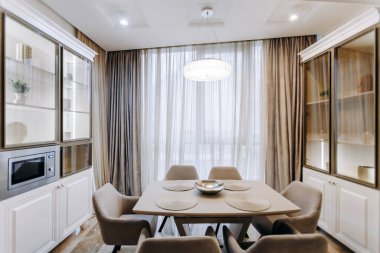 Konforlu bir yemek odasında geniş bir pencerenin önünde stratejik olarak dizilmiş güzel bir masa ve rahat sandalyeler bulunur.