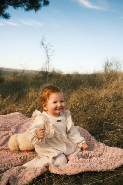 A joyful child is happily sitting on a cozy blanket in a beautiful, picturesque outdoor setting full of life