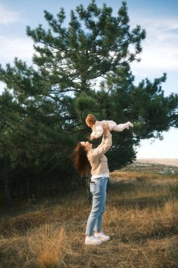 A mother joyfully lifts her child amidst a lush green landscape, capturing a sweet moment of connection.