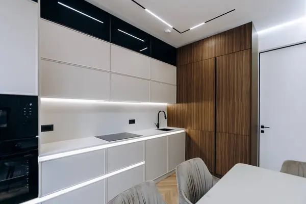 Zarif beyaz dolapların bulunduğu şık bir mutfak. Sıcak ahşap duvarlar, güzel bir masa ve yemek için rahat sandalyelerle tamamlanmış.