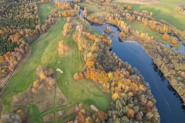 Sonbaharda çok renkli ağaçların havadan görünüşü, ve yeşil çimenler, orman, vahşi doğa, nehir, zıtlıklar. Köyde güzel bir sonbahar. Golf sahası. 