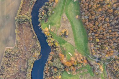 Sonbaharda çok renkli ağaçların havadan görünüşü, ve yeşil çimenler, orman, vahşi doğa, nehir, zıtlıklar. Köyde güzel bir sonbahar. Golf sahası. 