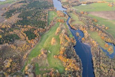 Sonbaharda çok renkli ağaçların havadan görünüşü, ve yeşil çimenler, orman, vahşi doğa, nehir, zıtlıklar. Köyde güzel bir sonbahar. Golf sahası. 