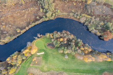 Sonbaharda çok renkli ağaçların havadan görünüşü, ve yeşil çimenler, orman, vahşi doğa, nehir, zıtlıklar. Köyde güzel bir sonbahar. Golf sahası. 