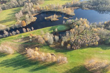 Havadan güzel bir sonbahar sabahının panoramik manzarası, golf sahası, nehir, çok renkli ağaçlar ve yeşil çimenler, sıcak güneş ışığı, gölgeler.