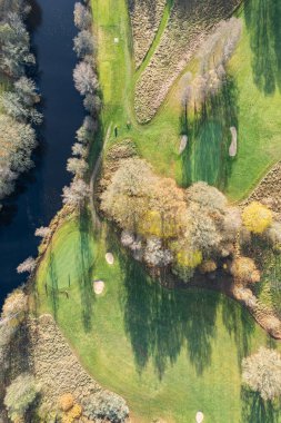 Havadan güzel bir sonbahar sabahının panoramik manzarası, golf sahası, nehir, çok renkli ağaçlar ve yeşil çimenler, sıcak güneş ışığı, gölgeler.