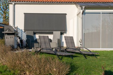 Güneşli bir günde verandada iki iskemle ve ızgara, dinlenme bölgesi. Sıcak ve rahat bir atmosfer.