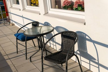 Güneşli bir günde verandada küçük masa ve sandalyeler, dinlenme bölgesi. Sıcak ve rahat bir atmosfer.