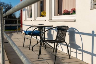 Güneşli bir günde verandada küçük masa ve sandalyeler, dinlenme bölgesi. Sıcak ve rahat bir atmosfer.