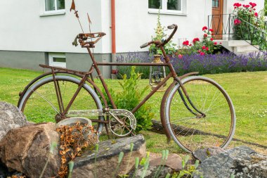 Sweden, Knislinge  July 5, 2022: Old rusty worn out bicycle in a yard of private house as a decoration. Unusual sculpture, concept, idea.