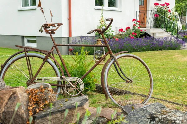 Sweden, Knislinge  July 5, 2022: Old rusty worn out bicycle in a yard of private house as a decoration. Unusual sculpture, concept, idea.