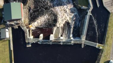 Aerial view on a big dam, barrage, weir in a city near a green and residential area on a sunny day. Water flowing.