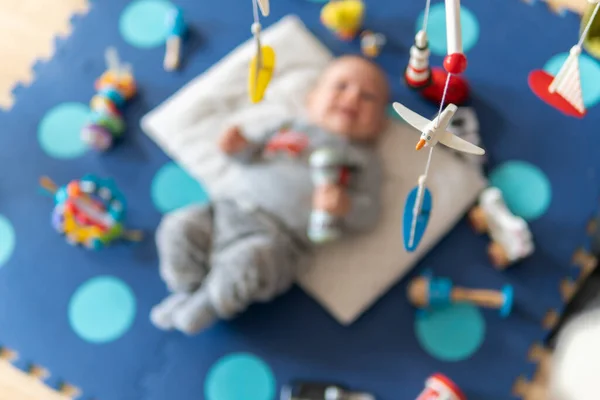 Hanging rotating wooden toy for babies. Newborn is having fun on a play mat.