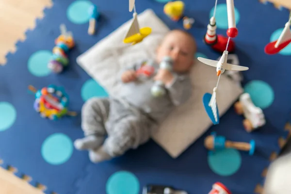 Hanging rotating wooden toy for babies. Newborn is having fun on a play mat.