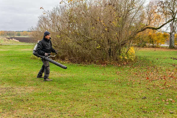 İsveç, Knislinge 26 Ekim 2022: Bir adam büyük bir hava üfleme makinesiyle düşen sonbahar yapraklarını temizliyor