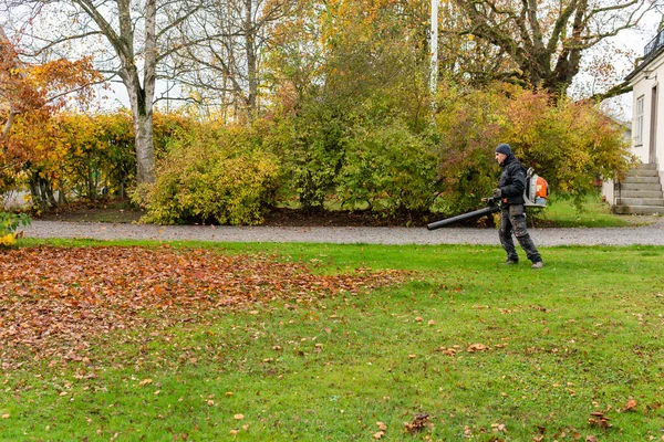 スウェーデン Knislinge 2022年10月26日 男は屋外の大きなブロワーマシンで秋の葉を掃除しています ストックフォト