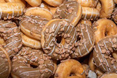 Tatlı ve lezzetli yuvarlak çörekler, şekerle kaplı halka çörekler. Çikolatalı donutlu donut. Şekerin sembolü, kızarmış hamur. Bir sürü tatlı, sağlıksız yemek. Gıda atıkları, gıda üretimi.